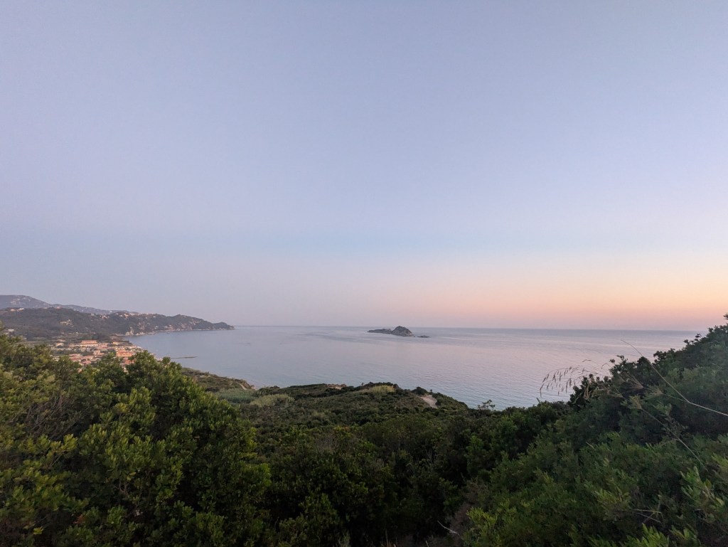 Vista panorámica de una costa tranquila al atardecer, con un mar sereno y una isla diminuta en el horizonte.